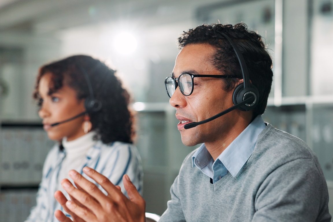 Consulting, contact us and support with man in call center for assistance, feedback or online help. Coworking, explain and headset with virtual assistant at desk in office for customer service