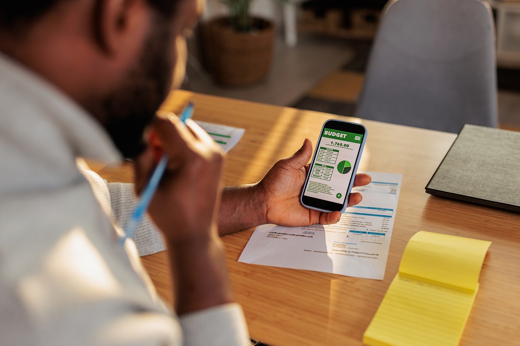 Man Reviewing Budget App And Bills While Planning Expenses At Home